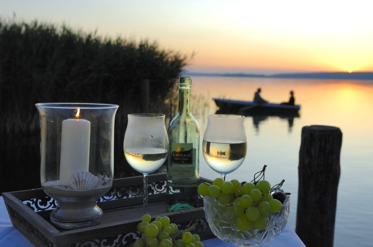 Sonnenuntergang auf der Seebrücke mit Blick auf ein Ruderboot bei einem Gläschen Wein